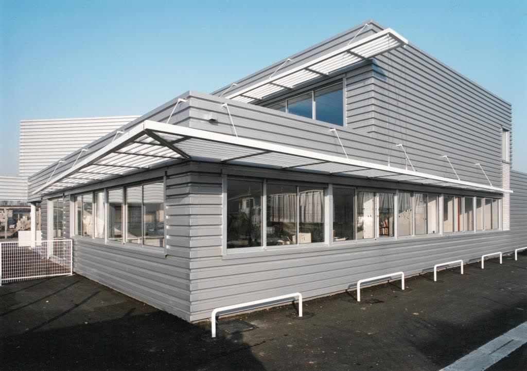 Bâtiment tertiaire en bardage métallique gris, toiture à redents vitrés